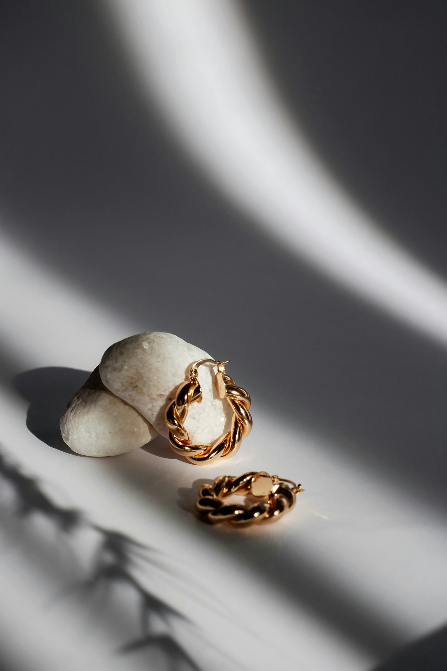 Gold hoop earrings on a textured surface with soft shadows